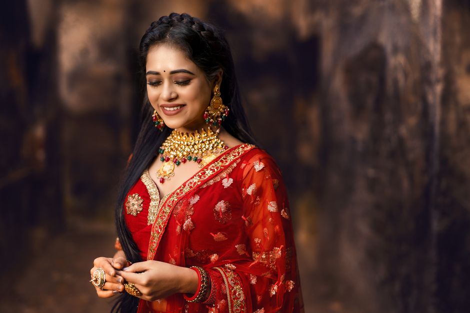 Portrait of a smiling Indian bride in a red saree with intricate jewelry, outdoors in Dhanbad, India.