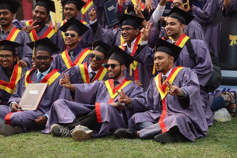 Group of university graduates celebrating with diplomas outdoors in Dhaka.