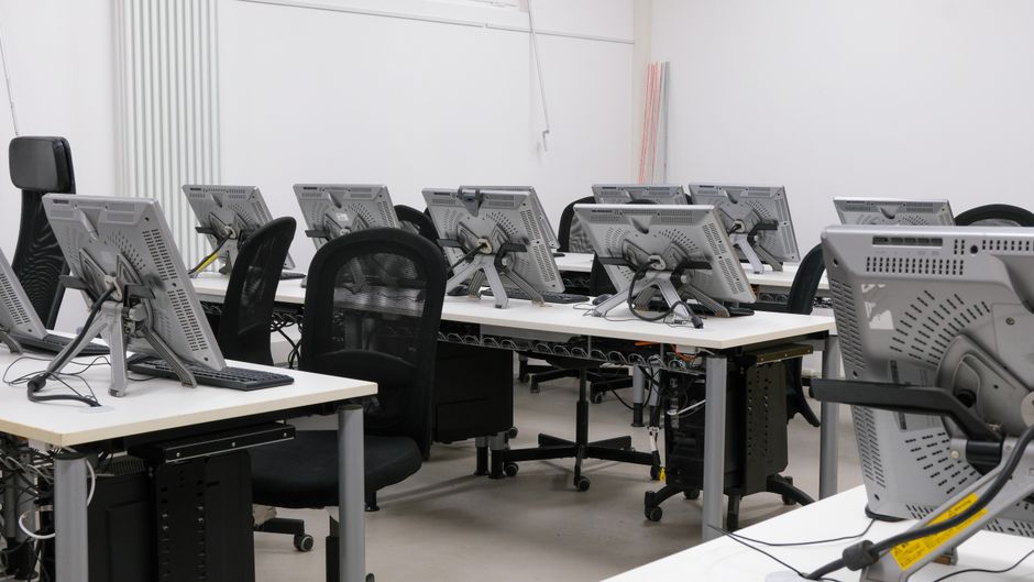 An empty computer lab featuring multiple workstations with monitors and chairs, ready for use.