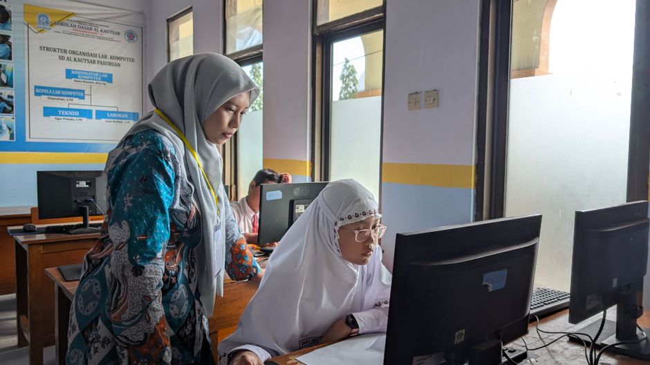 A female teacher guides a student working on a computer in a school lab, fostering learning.