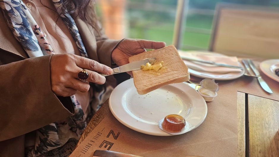 Person spreading butter on toast at a sunny cafe table.