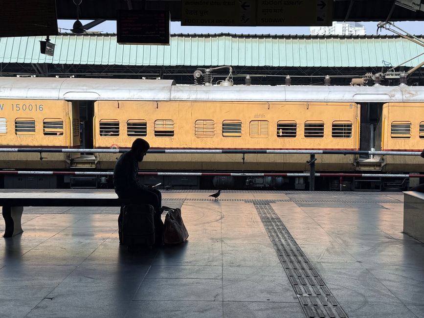 A person sitting on luggage at a train station platform with a yellow train in the background.