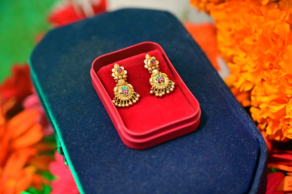 Close-up of intricate gold earrings in a red velvet box set against vibrant flowers.