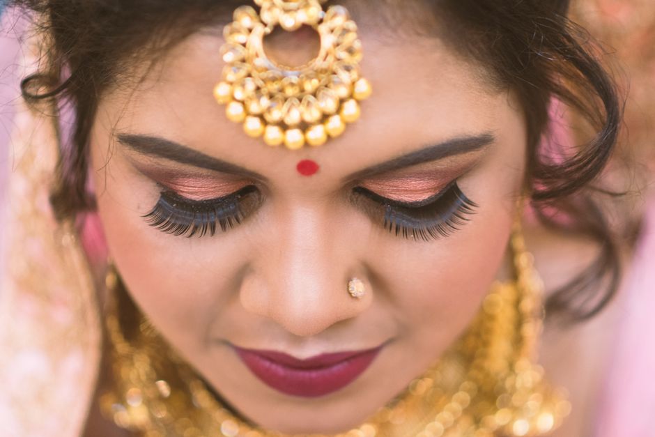 Close-up view of an Indian woman adorned with traditional bridal makeup and gold jewelry accentuating her features.