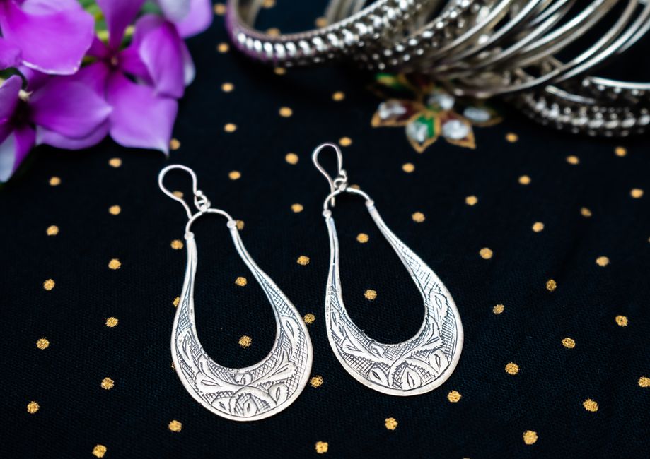 Stylish silver earrings displayed on black polka dot fabric with floral accents, ideal for luxury fashion.