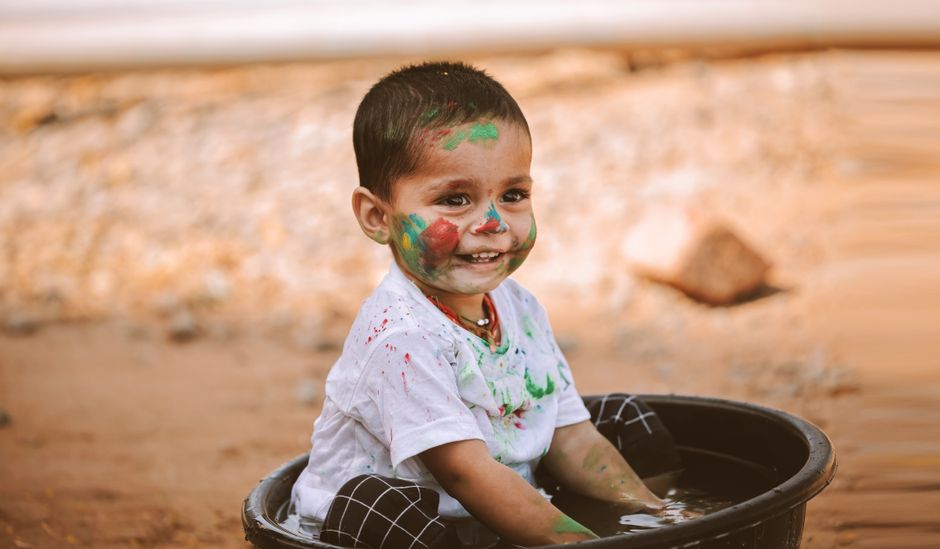 Happy child with colorful face paint playing in a basin outdoors, smiling with joyful expression.