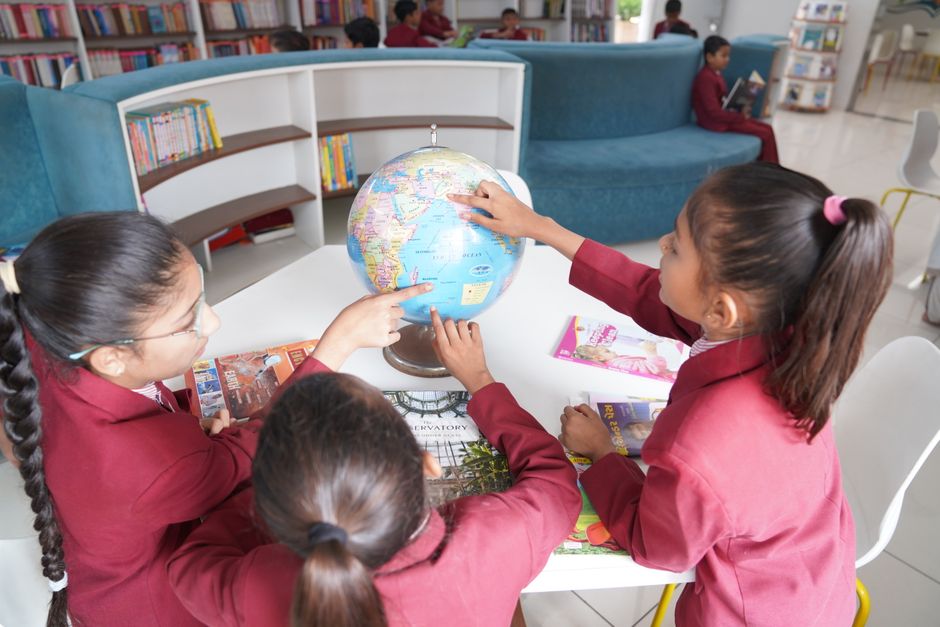 Children in uniform learning geography with a globe in a contemporary library.