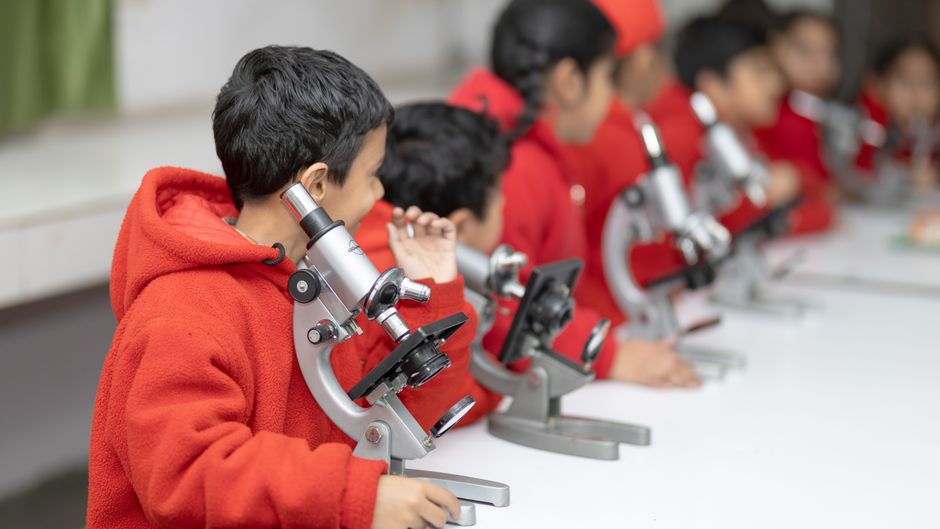 Young students in red exploring science with microscopes in a classroom setting.