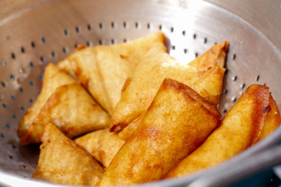 Close-up of golden fried samosas cooling in a metal colander, perfect snack.
